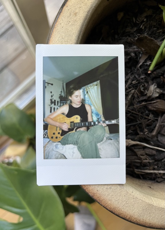 A polaroid of someone playing electric guitar, propped on a plant pot